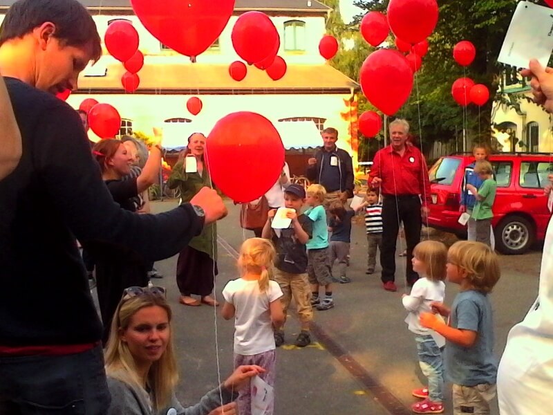 Kinder lassen gemeinsam mit ihren Eltern rote Luftballons in den Himmel steigen.